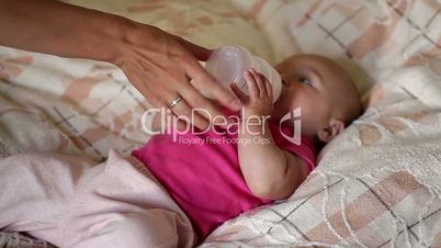 little baby lying on the bed and drinking milk from a bottle