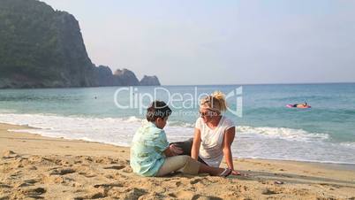 Mother and son sitting at beach and talking