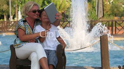 Mother and son sitting on a park bench and taking a selfie