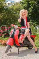 Frau posiert lachend im modischen Sommerkleid auf einem Motorroller