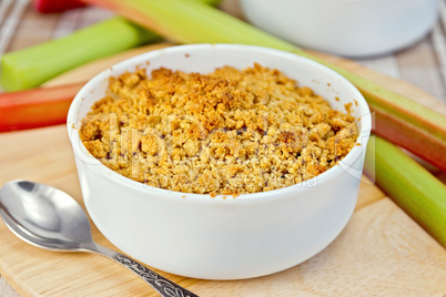 Crumble with rhubarb in bowl on tablecloth and board
