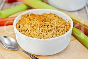 Crumble with rhubarb in bowl on tablecloth and board
