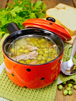 Soup from green peas with meat in red bowl and bread on board
