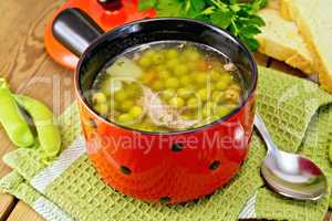 Soup from green peas with meat in red bowl on napkin