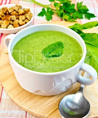 Soup puree with spinach leaves and spoon on fabric