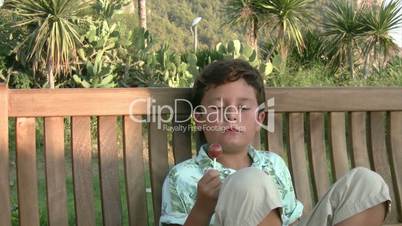 Young boy eating a lollipop on swing and smiling