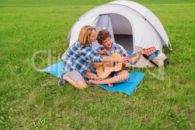 Teenage boy and girl near the tent play guitar