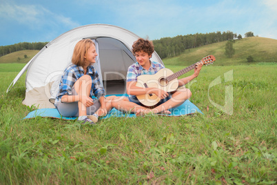 Teenage boy and girl near the tent play guitar