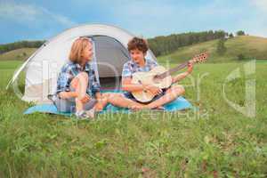 Teenage boy and girl near the tent play guitar