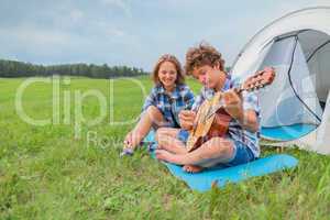 Teenage boy and girl near the tent play guitar