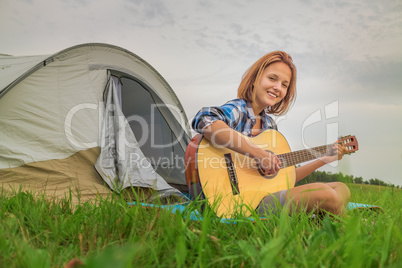 Teenage  girl near the tent playing a guitar
