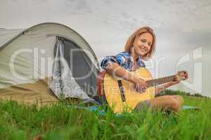 Teenage  girl near the tent playing a guitar