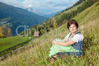 Woman in dirndl sitting on mountain meadow