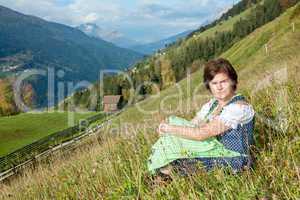 Woman in dirndl sitting on mountain meadow
