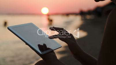 Girl working with tablet PC on beach at sunset