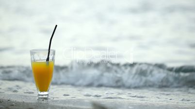 Glass of cocktail on beach and waves washing shore