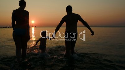 Parents playing ball with son in sea at sunset