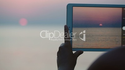 Taking pictures of sunset over sea with touch pad