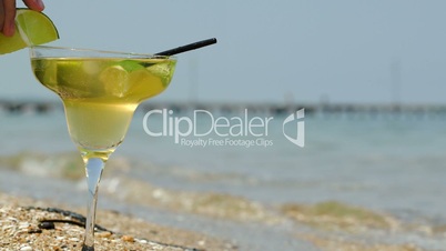 Putting lime slice on glass of cocktail by sea