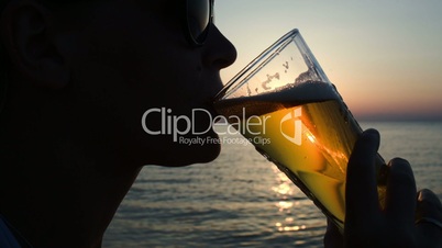 Woman drinking beer on beach at sunset