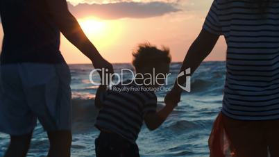 Happy family of three dancing by sea at sunset