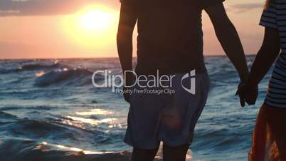 Loving couple holding hands by rough wavy sea at sunset