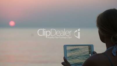 Woman making photo of sunset using tablet PC
