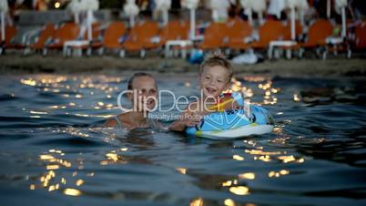 Son with rubber ring and mother bathing in sea