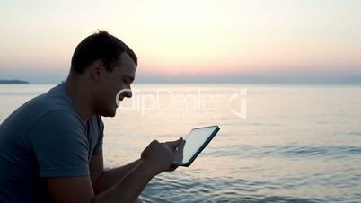 Young man by the sea typing message on pad