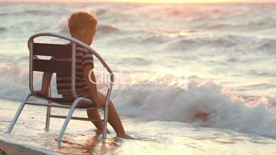 Boy sitting alone on the chair by sea