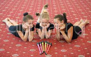 Three girls on the floor looking at Indian clubs
