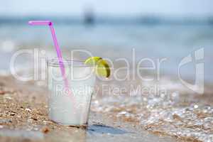 Glass of lemonade or water on beach by sea