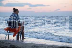 Woman sitting on chair by sea and using pad