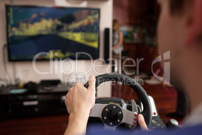 Man playing racing game with steering wheel simulator