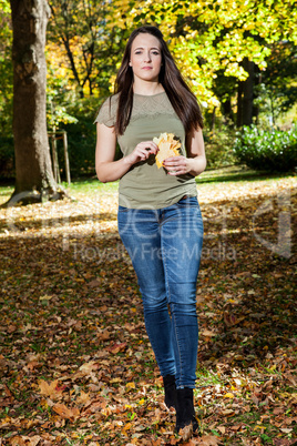 Woman walking in autumnal park and collect leaves