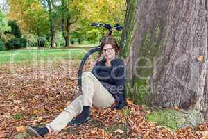 Woman with bicycle sitting in the leaves in autumnal park