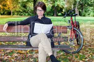 Woman with bicycle sitting in the park and reads