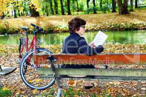 Woman with bicycle sitting in the park and reads
