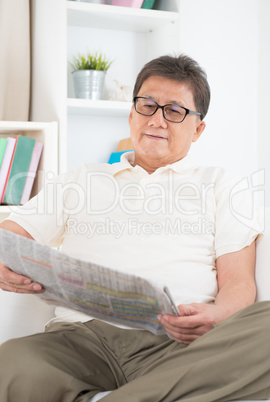 Mature Asian man reading newspaper