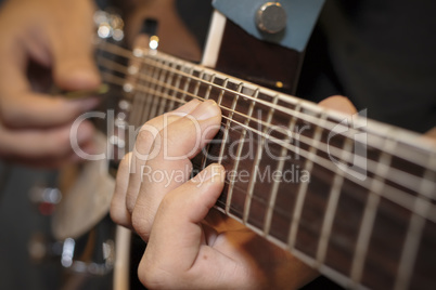 Close up shot of a man with his fingers on the frets of a guitar