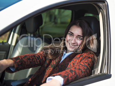 Young pretty smiling girl sitting behind the wheel of a car