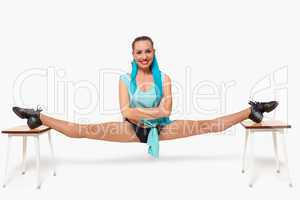 A girl sits in a pose of twine between two stools