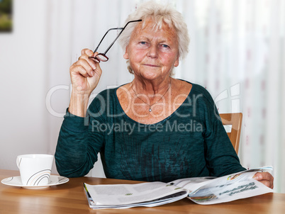 Elderly woman with cup looks up from reading
