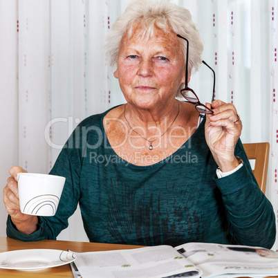 Elderly woman with cup looks up from reading