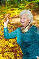 Senior woman poses with autumn leaves in the park