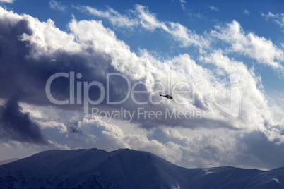 Helicopter in cloudy sky and winter mountains