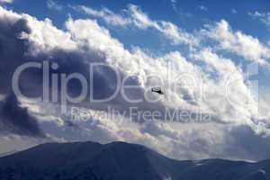 Helicopter in cloudy sky and winter mountains