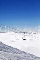 Ski slope, chair-lift and mountains under clouds