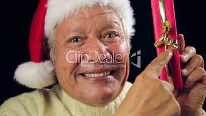 Jolly Old Man With Santa Cap Pointing At Red Gift