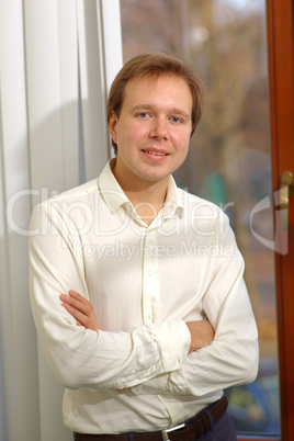 Happy young man standing by the window with blinds